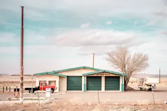 An abandoned gas station in an arid landscape with an old red truck and a caravan.