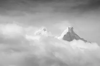 Two snow-covered mountain peaks protrude through a blanket of cloud.