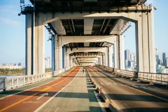 Single cyclist on a bridge with a separate cycle and pedestrian path and road, framed by tall city buildings in the background.
