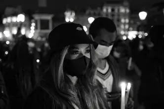 Close-up of a woman and man wearing masks and holding candles in a city at night.