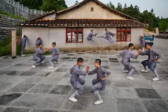 Shaolin monks practise martial arts in the courtyard in front of a traditional building