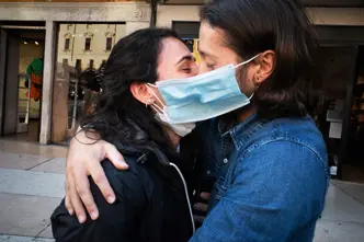 A couple wearing face masks hug and kiss in a street
