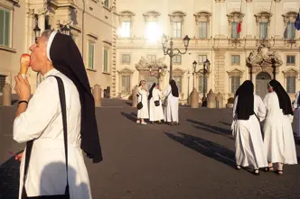A nun eats an ice cream while several nuns talk in the background.