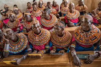Women from the Samburu tribe in Kenya sitting on a wooden bench in traditional clothes and smiling.