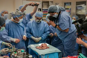A group of people in surgical gowns look at a mask representing a face, and some take pictures of it.