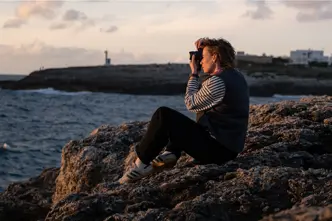 Julia Nimke is sitting on a rock by the sea with her Leica camera, taking photos