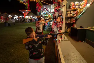 Child aiming at a carnival shooting game, capturing the vibrant atmosphere of a nighttime fairground and family entertainment.
