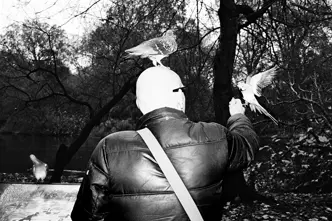 Black and White photo of man feeding birds in a park.