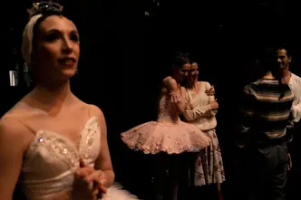 Ballet dancers embracing backstage after a performance while others wait in the wings.