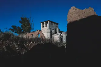 Historic stone ruins and a tower rise from a rugged landscape beneath a deep blue sky, framed by dramatic light and shadow.