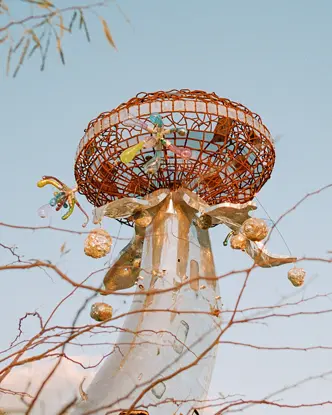 Metallic sculpture with colourful details in front of a blue sky and branches.