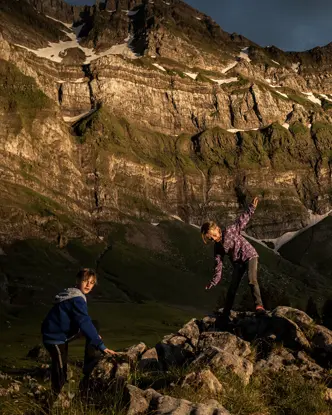 Two children climbing rocks in a mountain landscape at sunset.