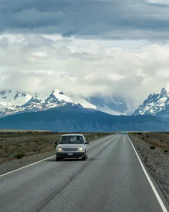 A car is driving on a road with snow-covered mountains in the background.