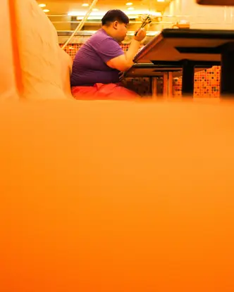Close-up of an orange bench in a restaurant with a person sitting and eating in the background.