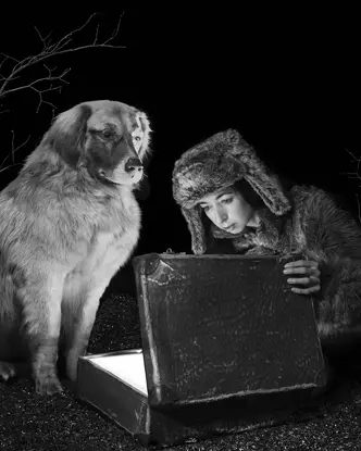 Viktoria Sorochinski and a dog looking into an old suitcase that is glowing inside. 