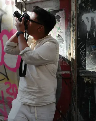 Patrick Domingo takes a photo standing in front of a graffiti wall.