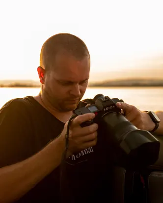Tino Scherer looking at his camera. In the background is a sea at sunset.