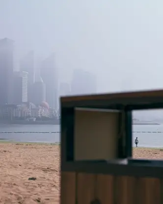 View through the rectangular opening of a garbage can on the beach with skyscrapers in the foggy background.