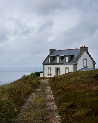 White house on a cliff, surrounded by flowers and a view of the cloudy sea.