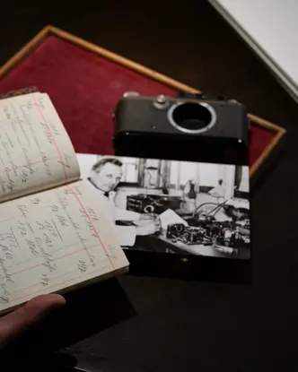 Person holding an old paper notebook, a photograph and a camera lie on the table.