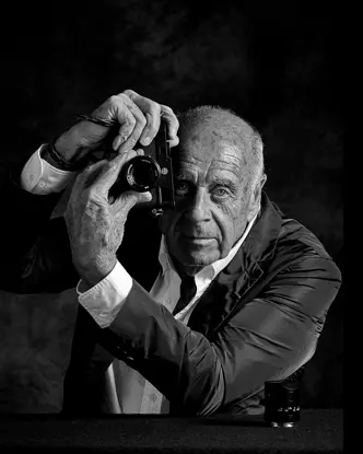 Elderly man holds a camera in front of his face and turns the lens of the camera.