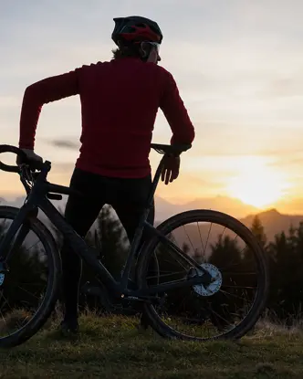 Man leaning on his mountain bike looking at the mountains at sunset.