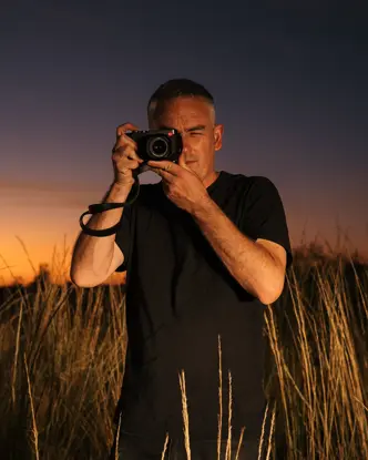 Person in a field with tall grass taking photos with a camera at sunset.