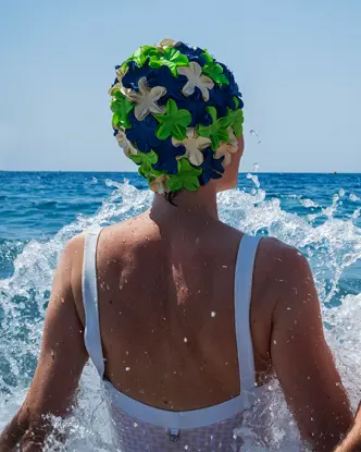 Two people in swimsuits and colorful bathing caps sitting in splashing water in the sea.