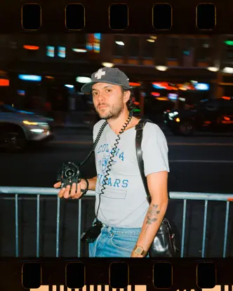 Joe Greer with a Leica M6 in his hand standing at a street at night.