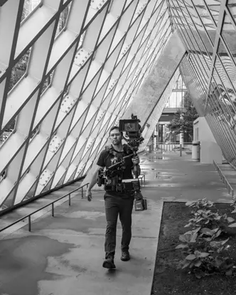 A cameraman walking with a professional camera setup in an architectural space.