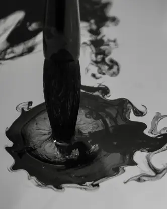 Brush dips into dark ink that spreads in the water.