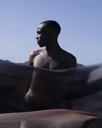 Man behind a transparent cloth looks to the side and light blue sky in the background.