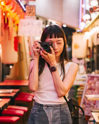 A woman takes pictures with a camera in a colorful, illuminated street.