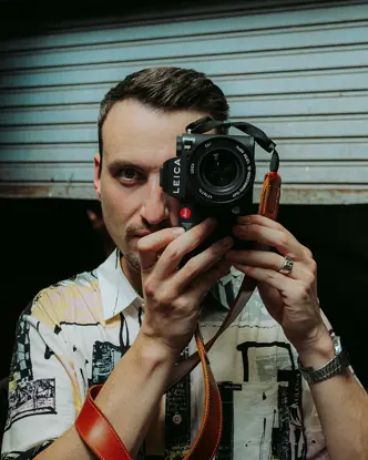 Philipp Reinhard looks through a camera and stands in front of a blue garage door.