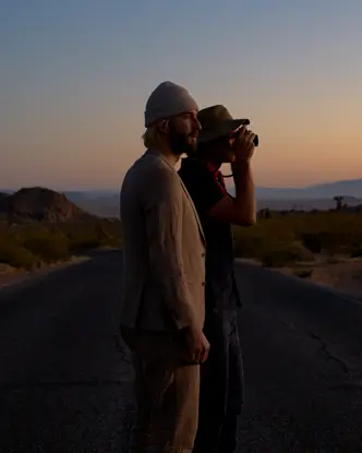 Garrett and Gantry Hill in a desert landscape at sunset, one looking through a camera.