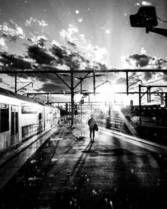 A person stands on a platform next to a train while the sun casts shadows.