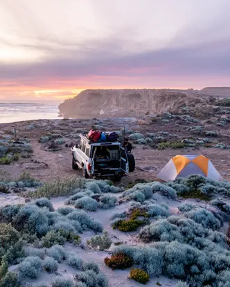 A jeep and two tents on a coast at sunset.