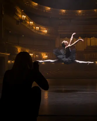 A person in the shade takes a picture of a ballerina jumping in an illuminated theatre.