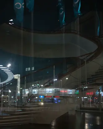 Reflection of a spiral staircase and a city at night in the glass front of a building.