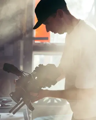 Person holds camera over a table with art materials, warm sunlight falls through window.