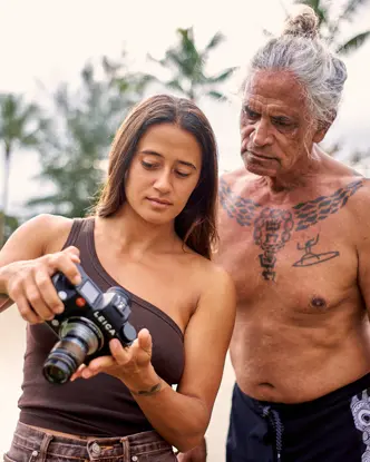 Mainei Kinimaka shows pictures on a camera to a man with Hawaiian tattoos on his upper body