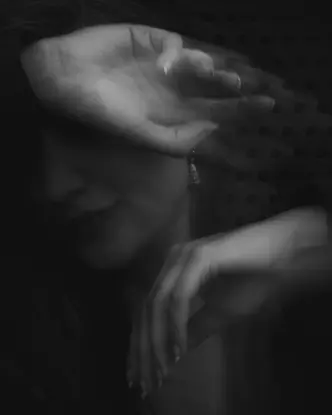 Blurred black and white image of a person covering her face with her arm.