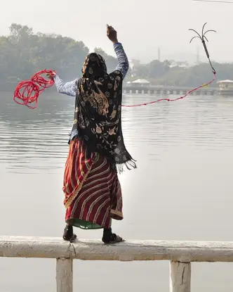 A woman and a child are standing on a railing in front of a lake and are fishing.