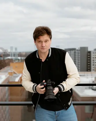 Person holding a camera, in the background are skyscrapers and a bridge on a cloudy day.