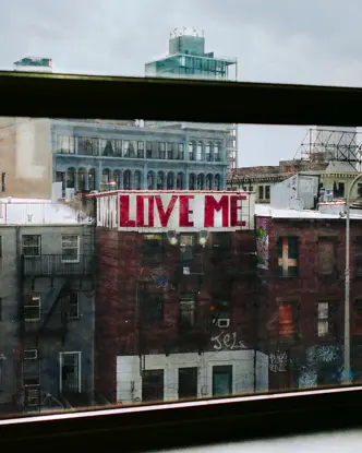View from a window of a city with a building bearing the graffiti ‘LOVE ME’.