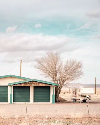 An abandoned gas station in an arid landscape with an old red truck and a caravan.