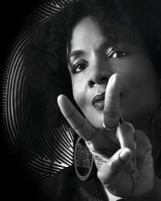 Black and white portrait of a woman with an Afro hairstyle making the peace sign