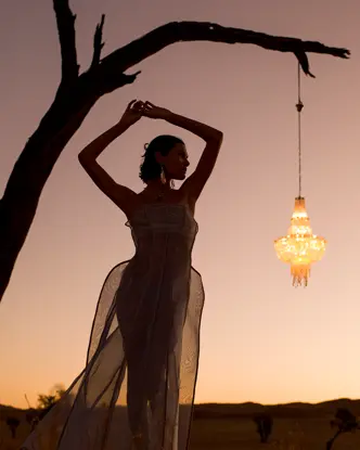 Woman posing under a tree at sunset next to a hanging lantern.