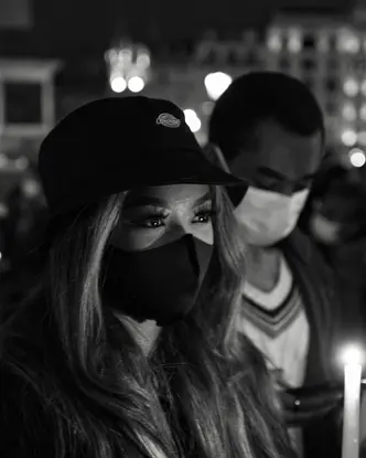 Close-up of a woman and man wearing masks and holding candles in a city at night.
