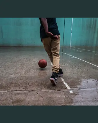 Person playing basketball on a wet court with a turquoise wall in the background.